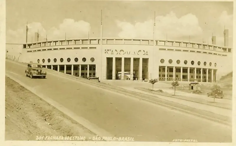 Cartão-postal antigo com a fachada do Estádio Municipal do Pacaembu e um automóvel na rua em frente